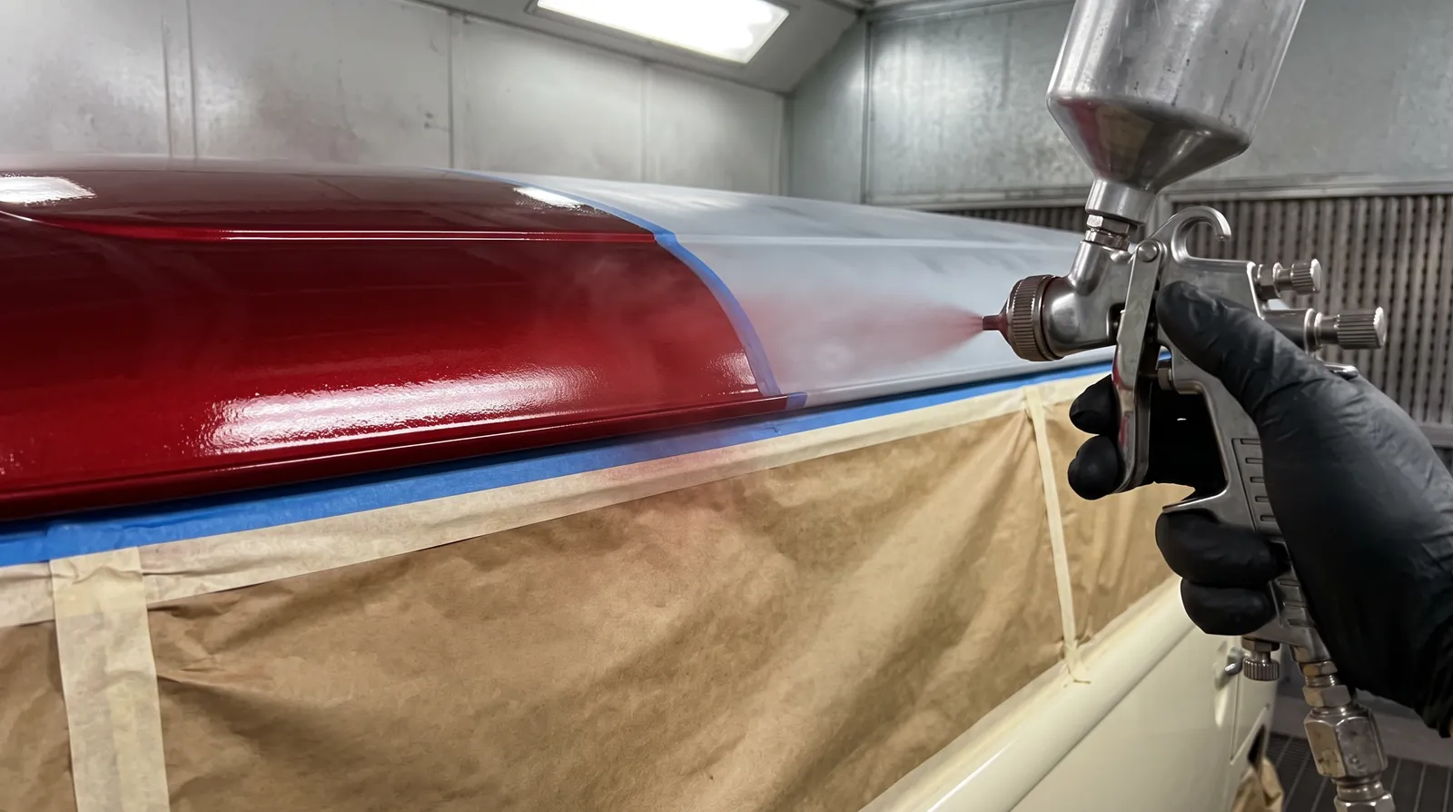 Red paint going on the top of a camper in the spray booth, the cream below it masked off