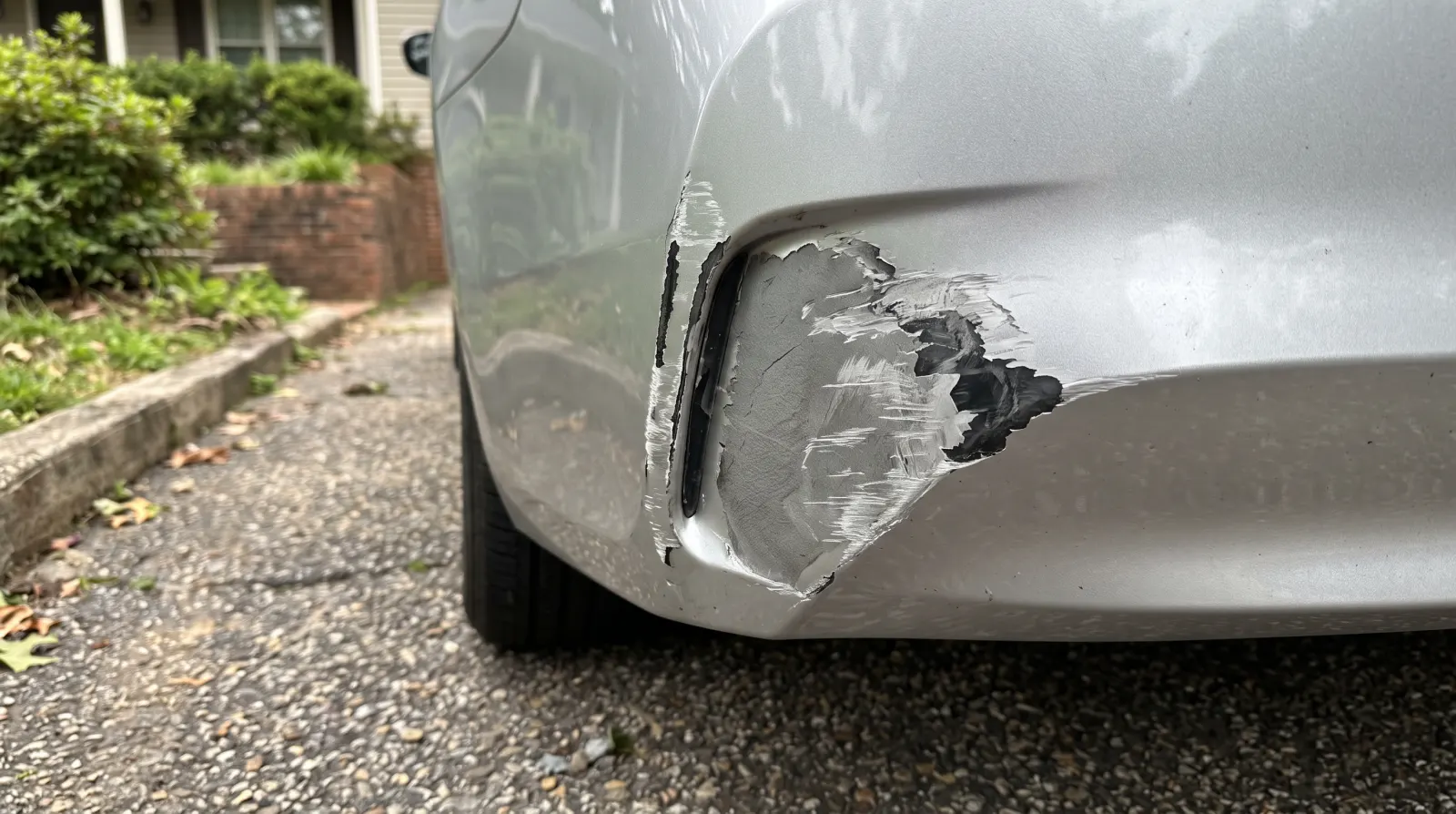 The corner of a silver bumper scraped through to the dark plastic, with a split running up beside the wheel arch