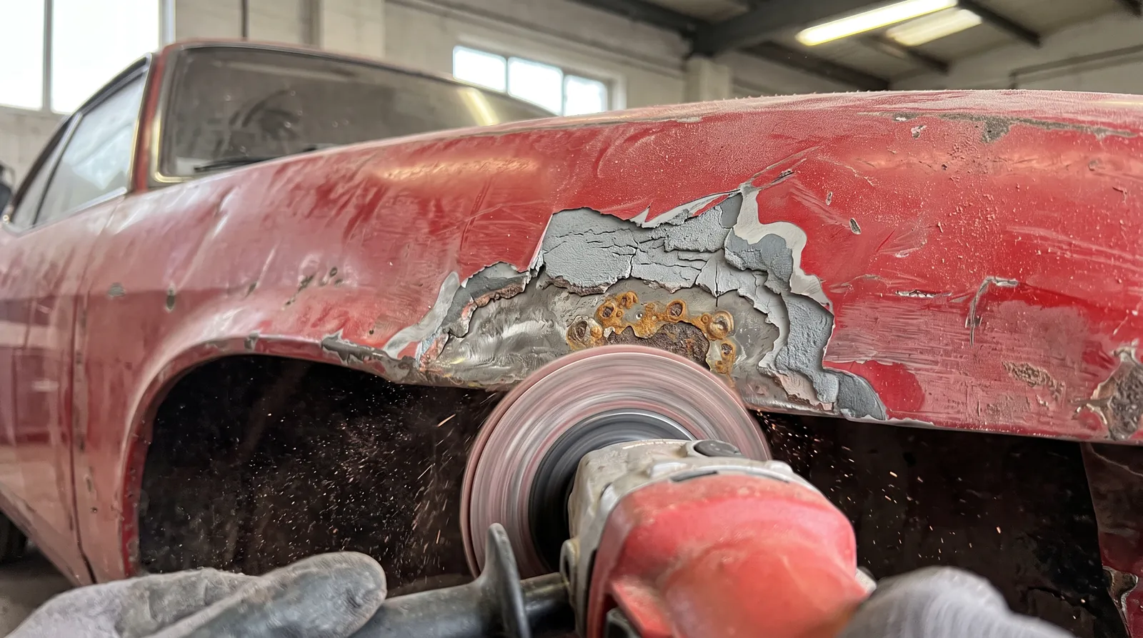 A grinder cutting rust back to clean steel on the wheel arch of a red classic