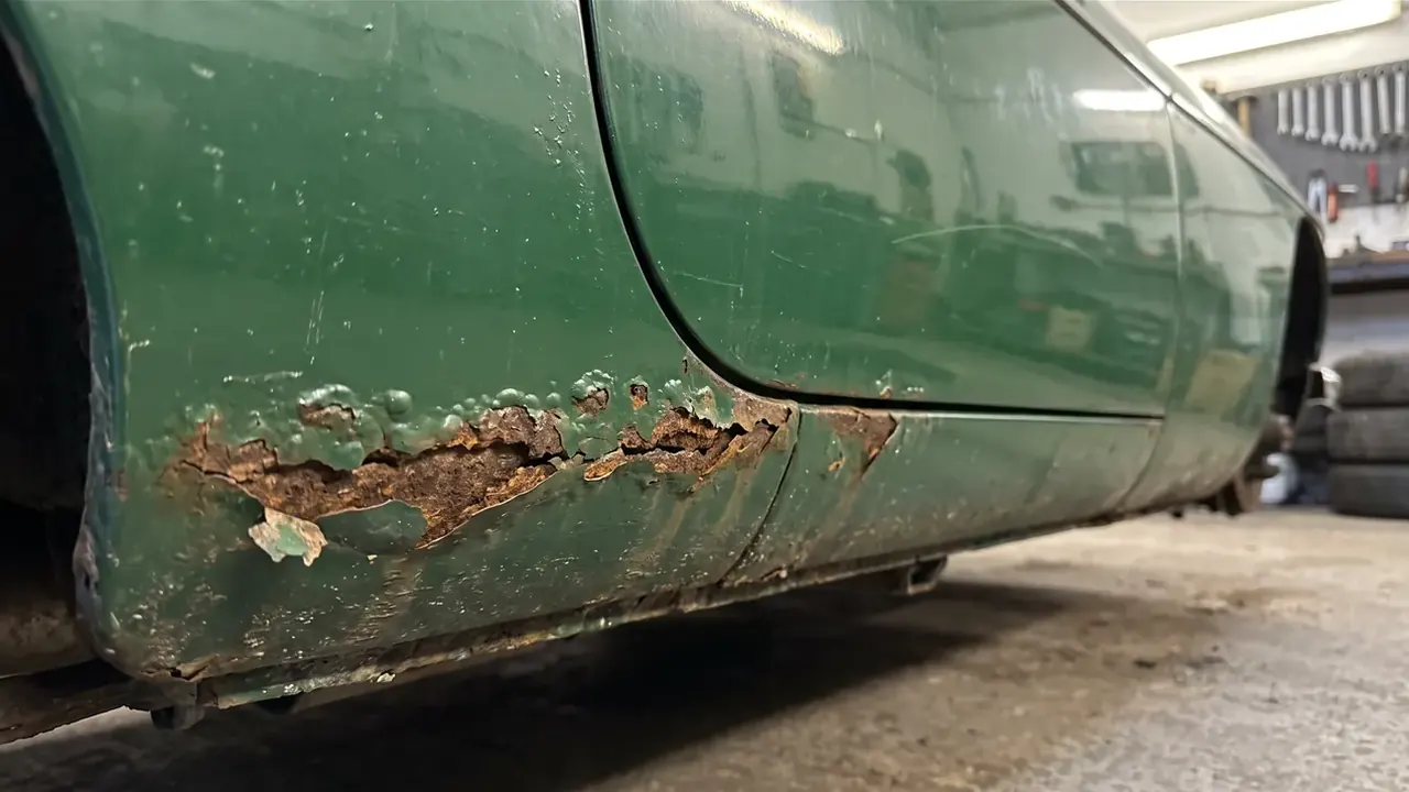 Paint bubbling and flaking off rust low down on a green classic