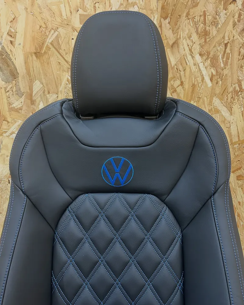 A black leather seat with blue double diamond stitching and an embroidered VW badge