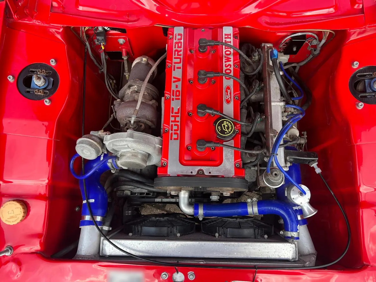 A Cosworth turbo engine in the red engine bay of a Ford Escort