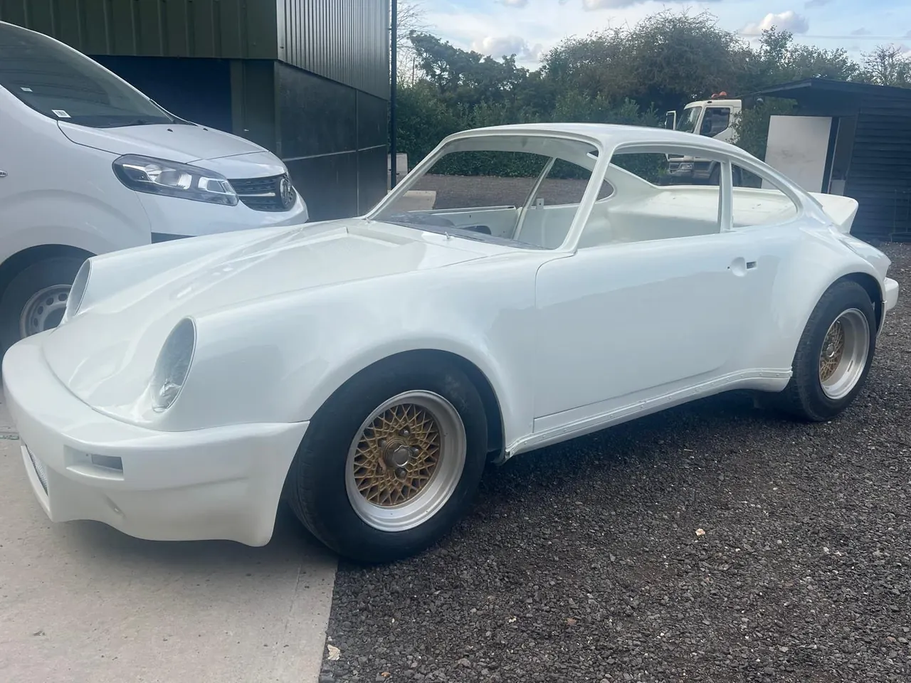 A white classic Porsche 911 shell on gold wheels in the yard
